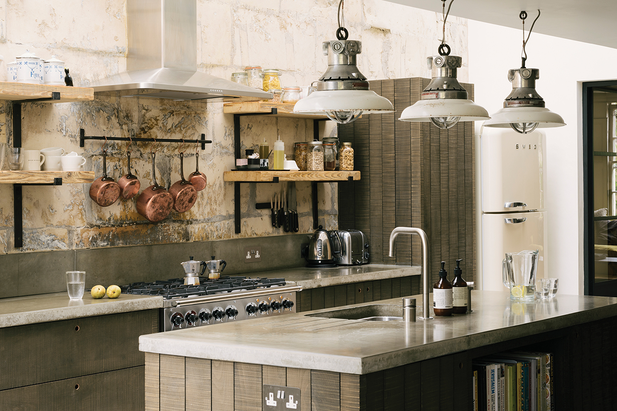 Farmhouse kitchen with band-sawn beech wood open shelving, concrete countertops, stained rough-sawn cabinetry, and natural stone walls.